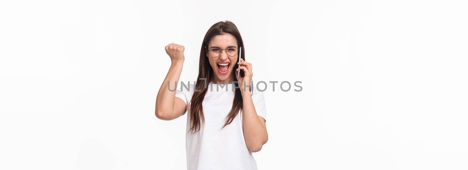 Communication, technology and lifestyle concept. Portrait of successful happy and excited woman winning, receive great news on phone, fist pump triumphing and saying yes, hold smartphone near ear by Benzoix