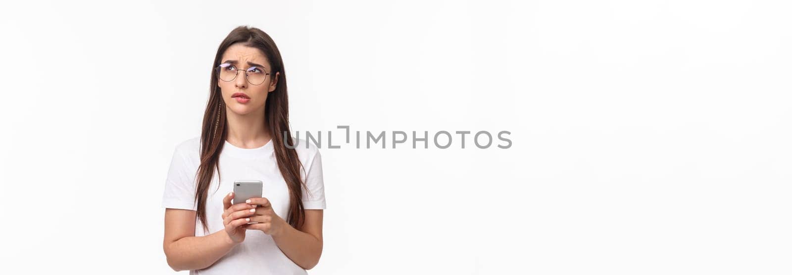 Communication, technology and lifestyle concept. Portrait of troubled and concerned young woman worried for friend, sending text message if shes okay and thinking, look up nervous, hold mobile phone.