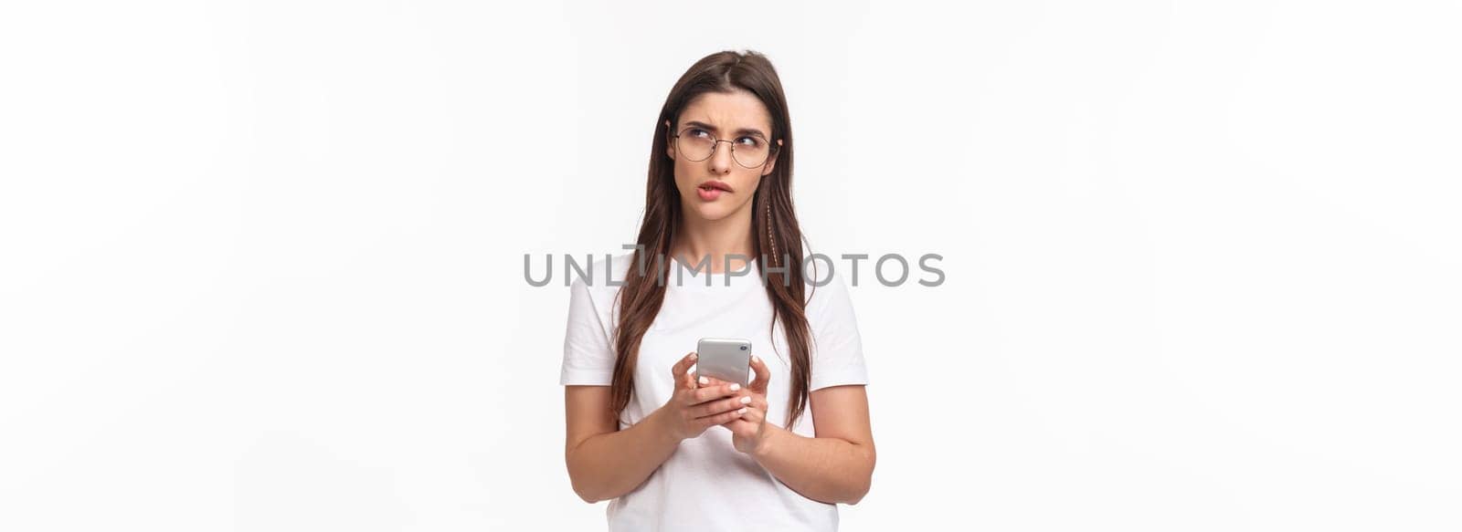 Communication, technology and lifestyle concept. Portrait of thoughtful young woman working remote, answer clients on phone, hold smartphone look up thinking what text back.