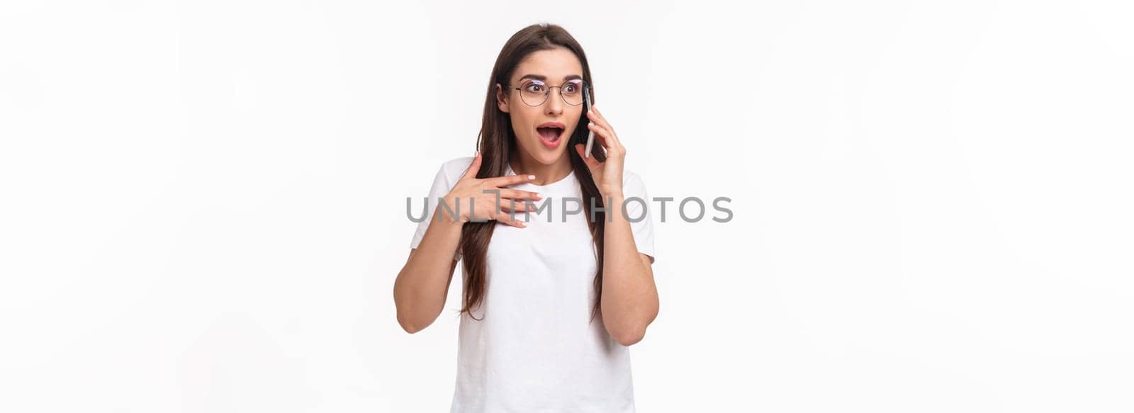 Communication, technology and lifestyle concept. Portrait of excited and surprised, overwhelmed young cute girl receive incredible news, gasping and touching heart as talking on phone, winning.