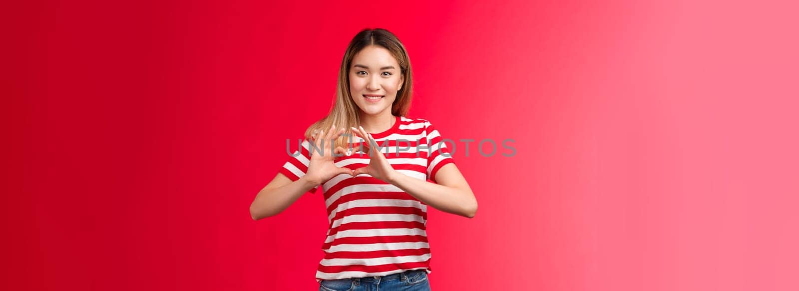 Asian girl express love and support lgbtq community. Heartwarming sweet tender blond female show heart sign near chest smiling friendly happily showing romantic attitude cherish relationship by Benzoix