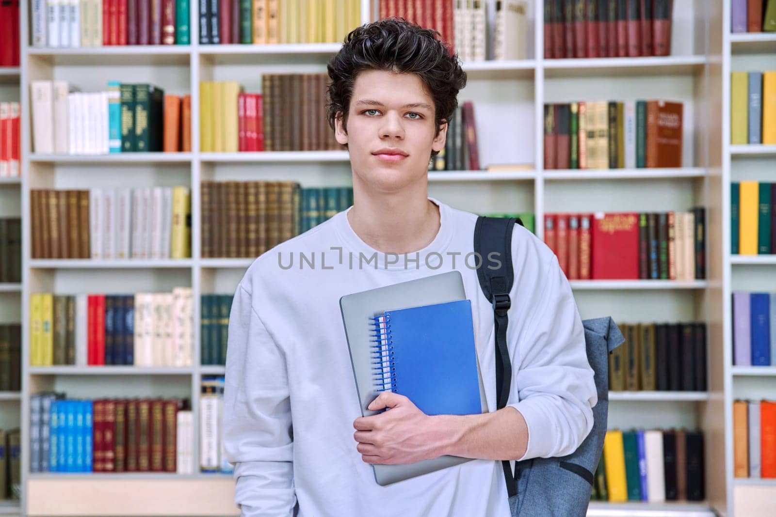 Portrait of confident handsome college student teenage male 19, 20 years old inside library of educational building. Education, youth, lifestyle concept