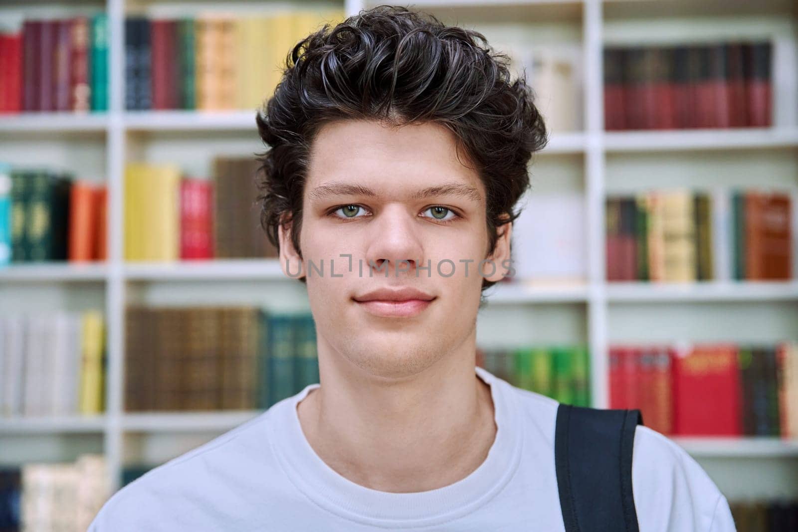 Headshot portrait of confident handsome college student guy with crossed arms inside library of educational building. Education, youth, lifestyle concept