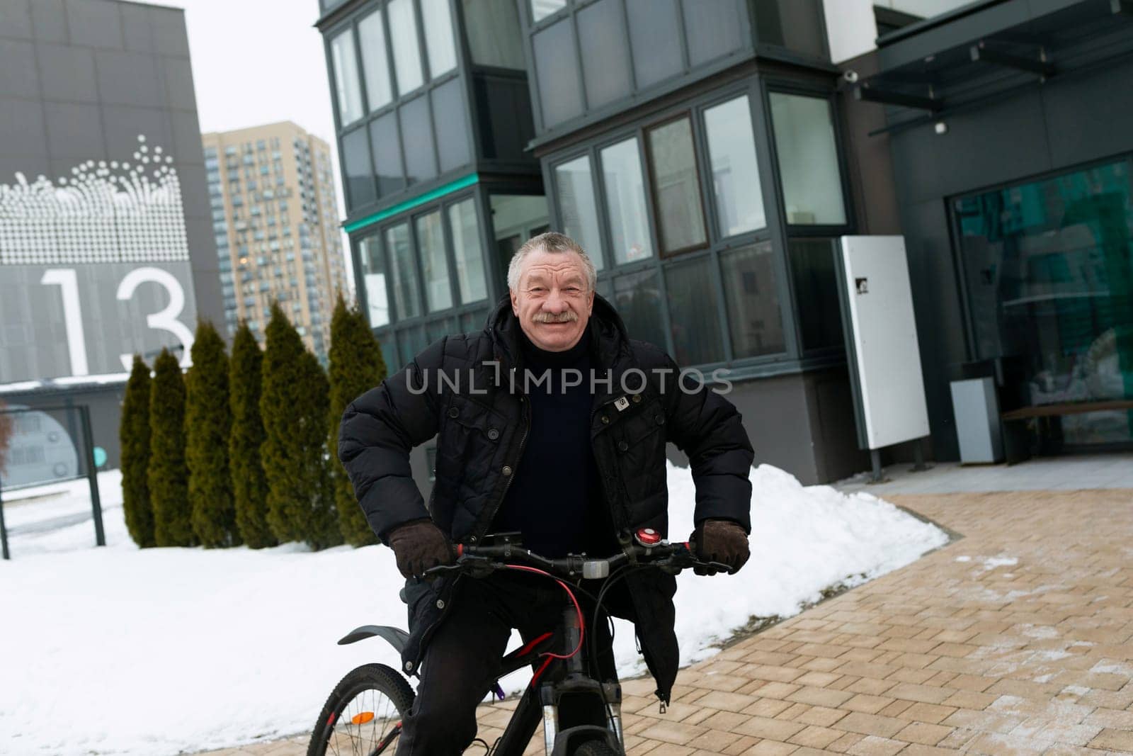 Senior man actively pedaling a bicycle on the street in winter.