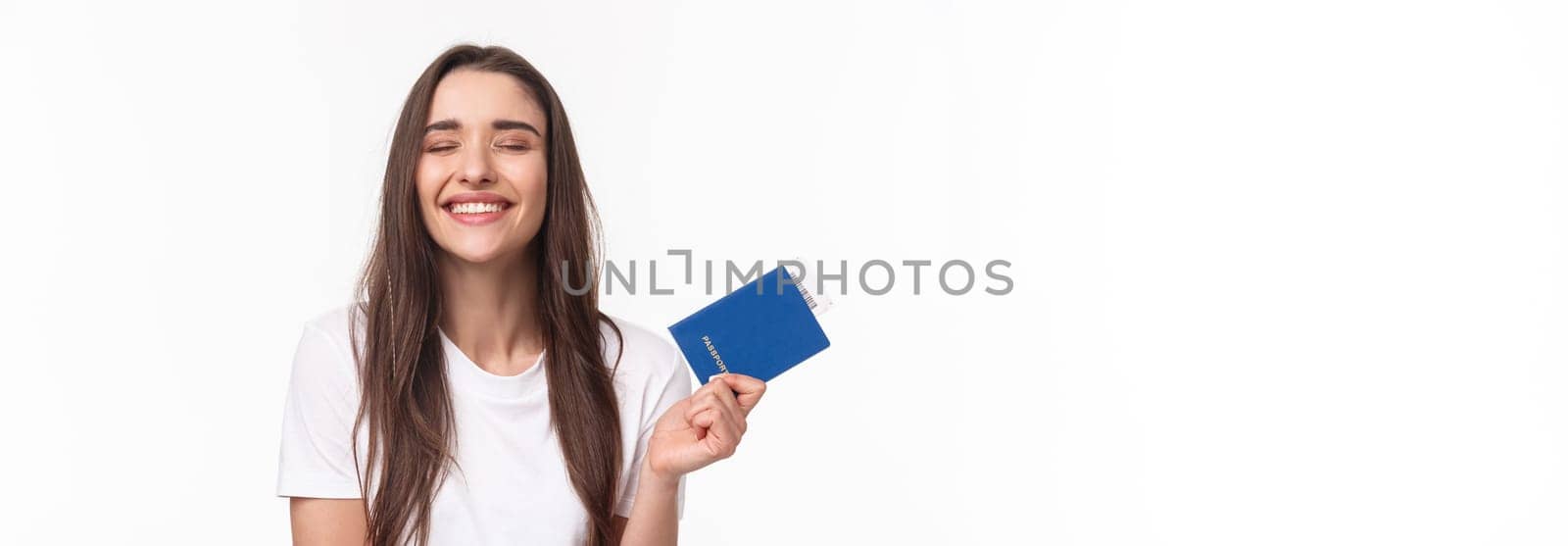 Travelling, holidays, summer concept. Dreamy happy young beautiful girl in white t-shirt, close eyes smiling, daydreaming how she sunbathing near beach on vacation, hold passport with ticket.