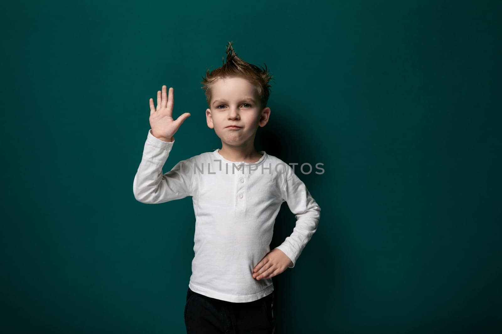 A young male child is standing in front of a vibrant green wall. He appears curious and engaged, perhaps examining the texture or color of the wall. The boy is wearing casual clothing and seems to be in a public space.