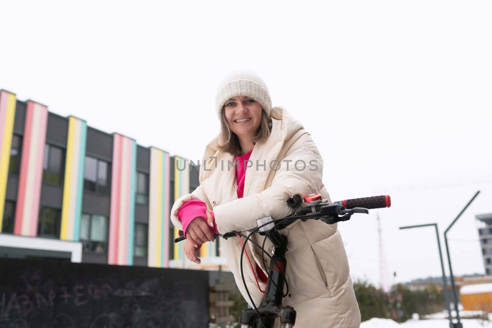 A woman wearing casual clothing rides a bike in front of a vibrant multi-colored building. The building features a variety of bright colors, creating a striking backdrop to the scene. The woman appears focused on her ride, with the colorful architecture adding interest to the urban environment.