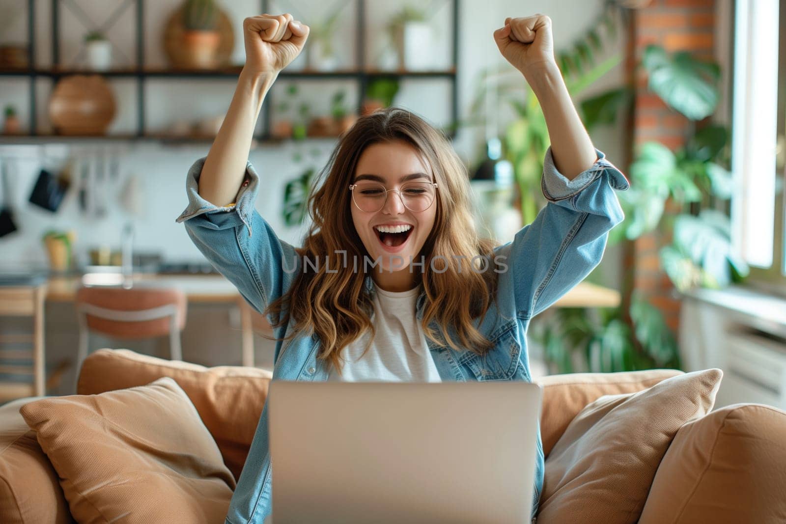 Happy overjoyed laughing woman celebrating success raising her hands up while working on laptop sitting at home office