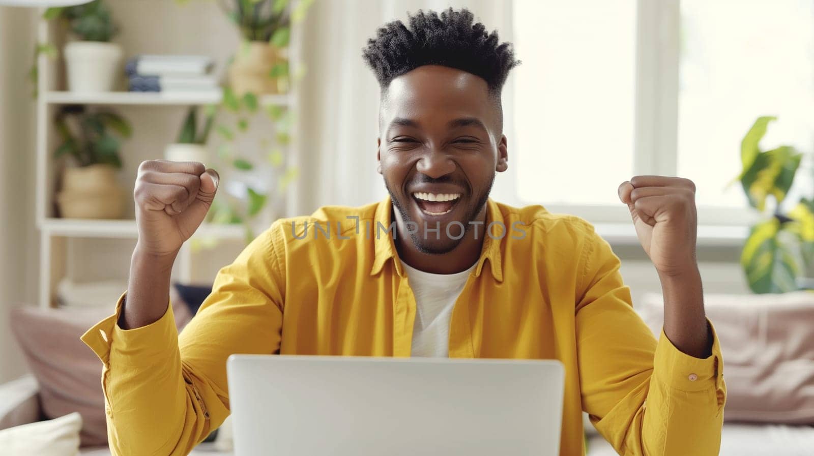 Happy overjoyed laughing african man celebrating success raising her hands up while working on laptop sitting at home office