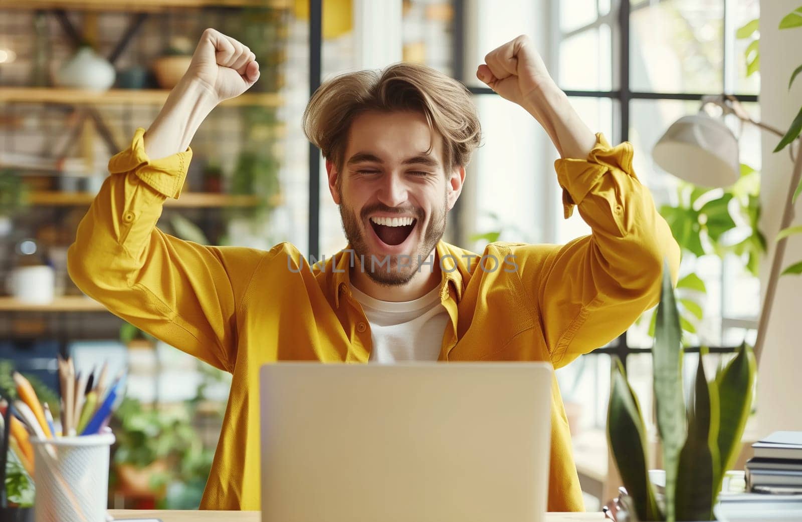 Happy overjoyed laughing man celebrating success raising her hands up while working on laptop sitting at home office