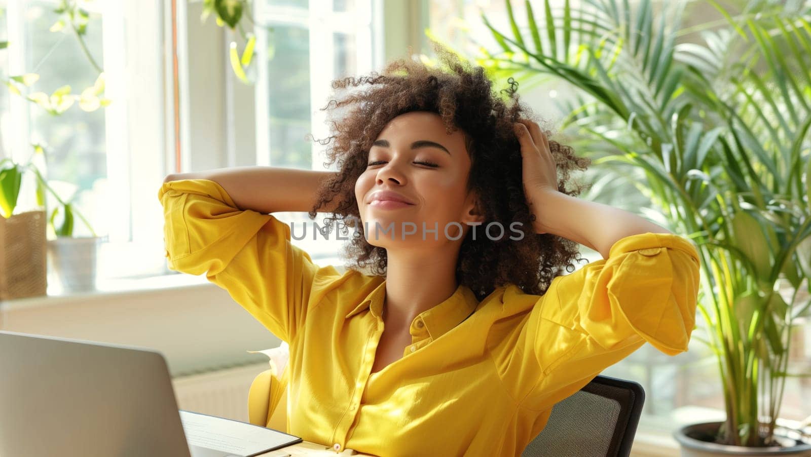 Happy relaxed young african woman enjoying sitting at desk during working at the laptop at home with green plants, female freelancer or student