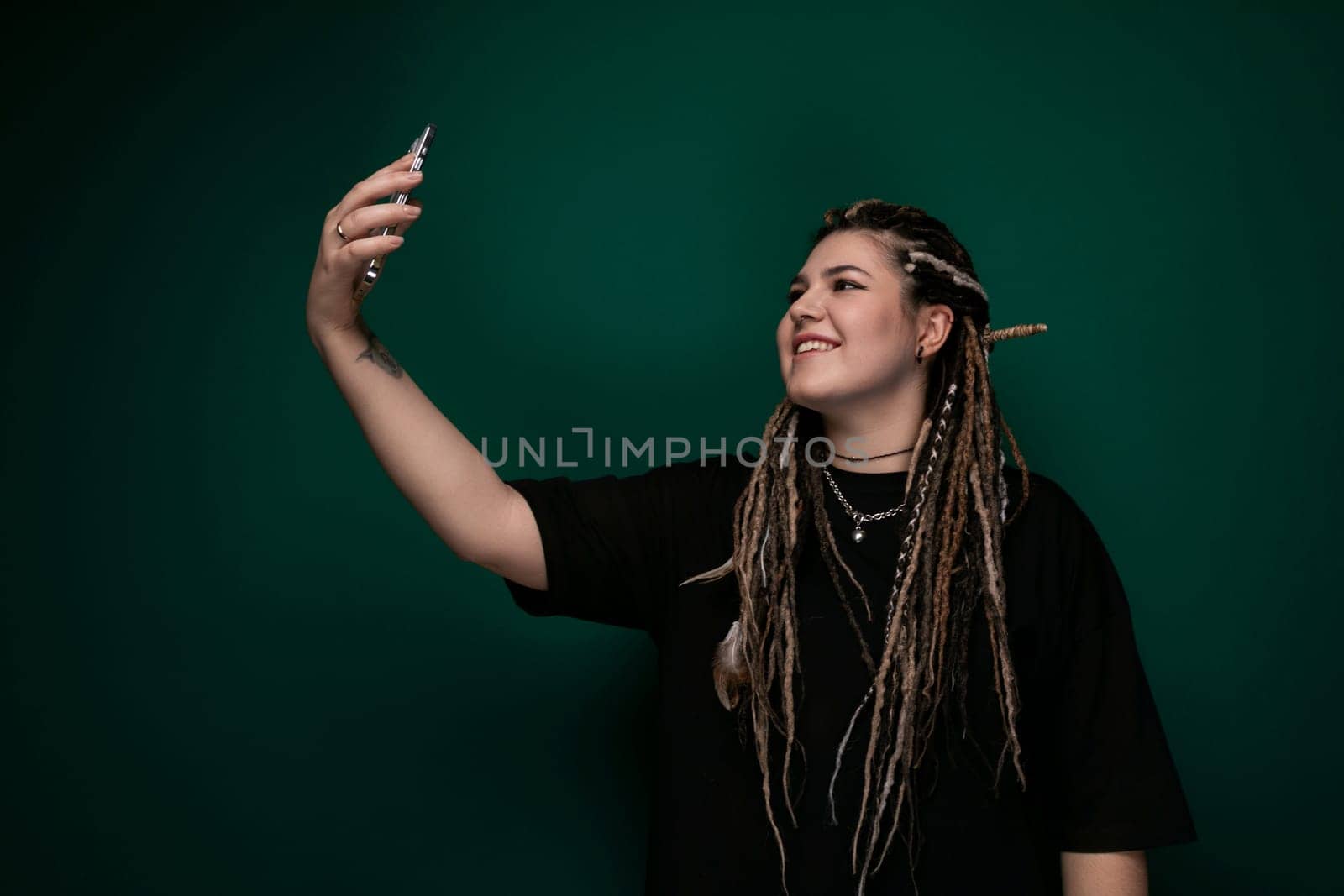 A woman with dreadlocks is seen holding a cell phone in her hand. She appears focused as she interacts with the device. Her distinctive hairstyle adds to her unique appearance.