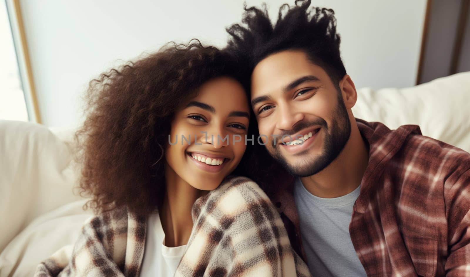 Portrait of happy smiling young couple hugging, cheerful woman and man sitting on sofa at home together