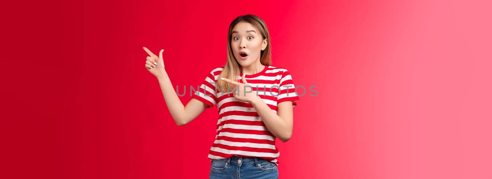 Surprised impressed attractive modern asian girl blond haircut open mouth gasping astonished, pointing right, show fingers impressive stunning promo new clothes collection look camera enthusiastic.