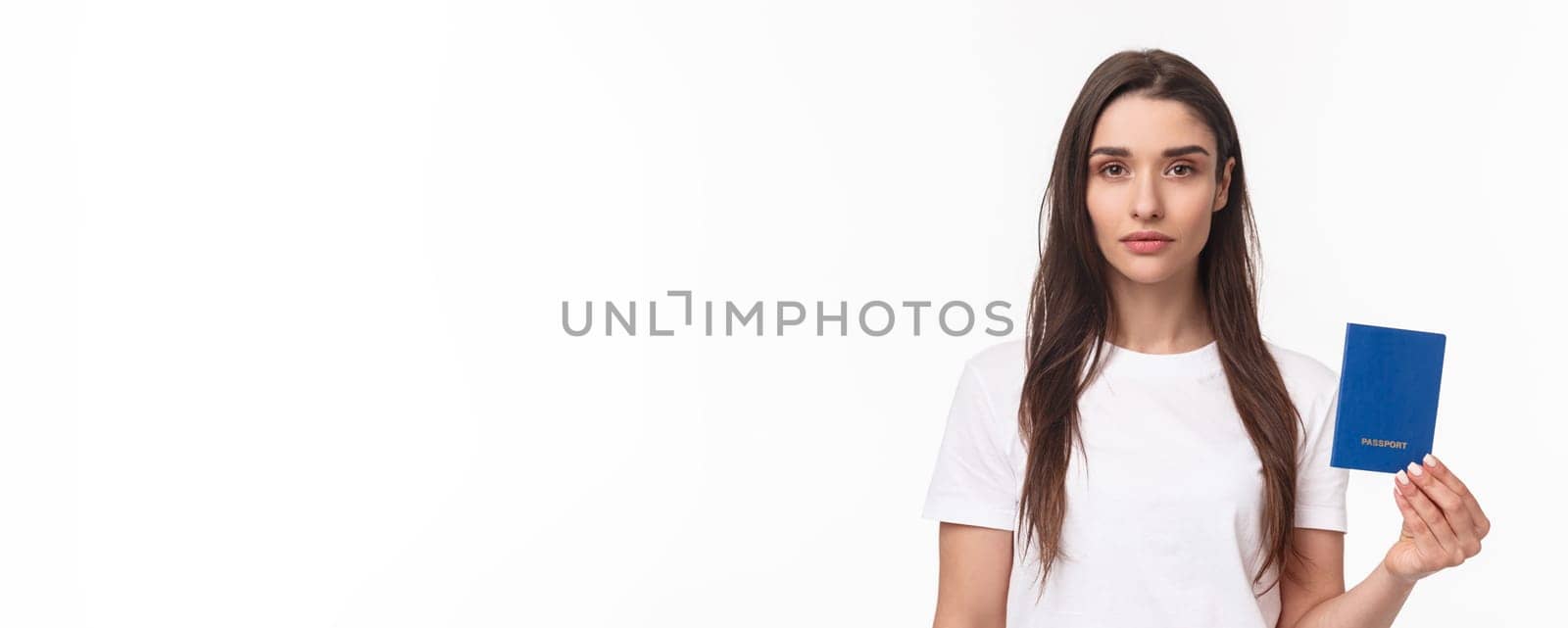 Travelling, holidays, summer concept. Serious-looking young confident girl showing her brand new passport, ready to travel abroad, packing up baggage, standing white background.