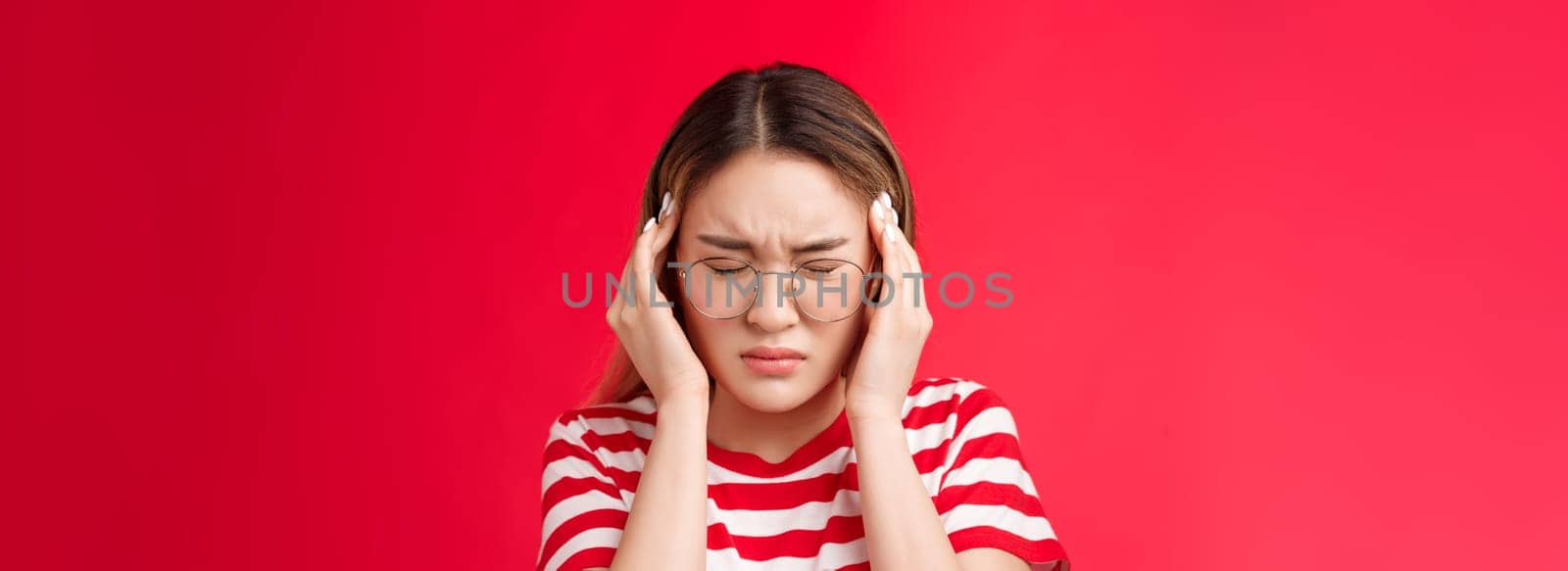 Close-up pressured distressed young asian woman grab head touch temples, frowning close eyes bend head suffering headache, feel terrible migraine, standing upset red background. Copy space