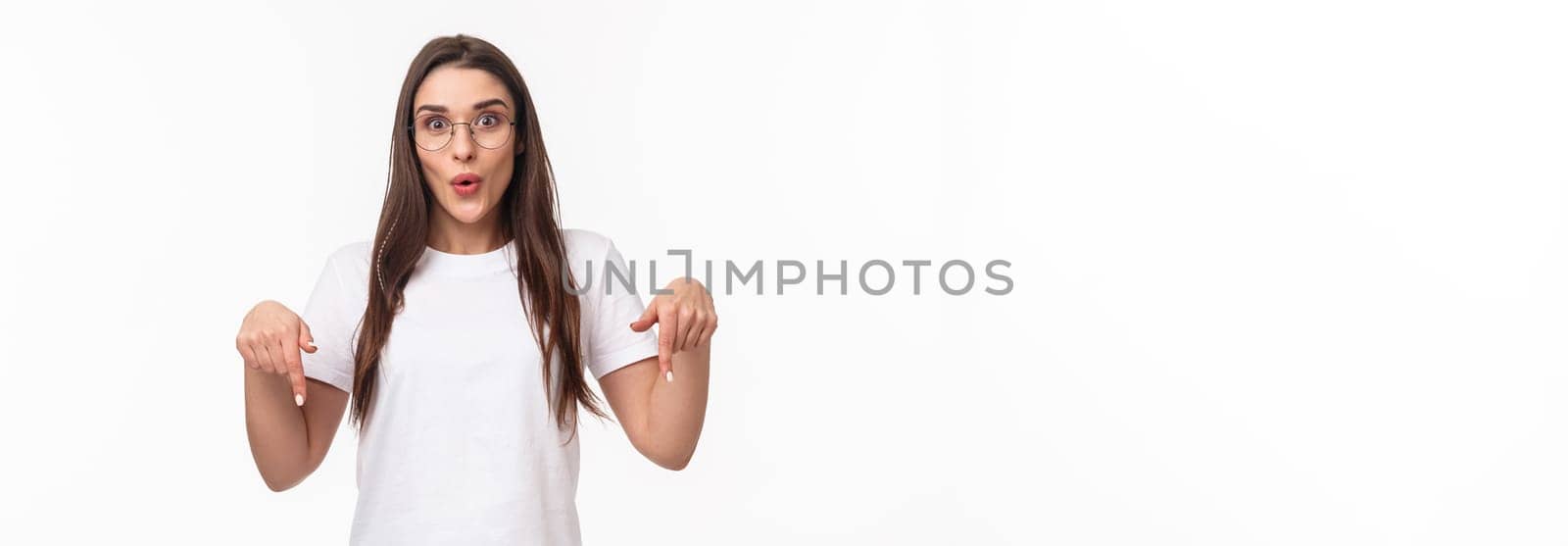 Portrait of amused and curious brunette female student inviting everyone check out very interesting event, follow this page or link, visit store, pointing fingers down, bottom advertisement.