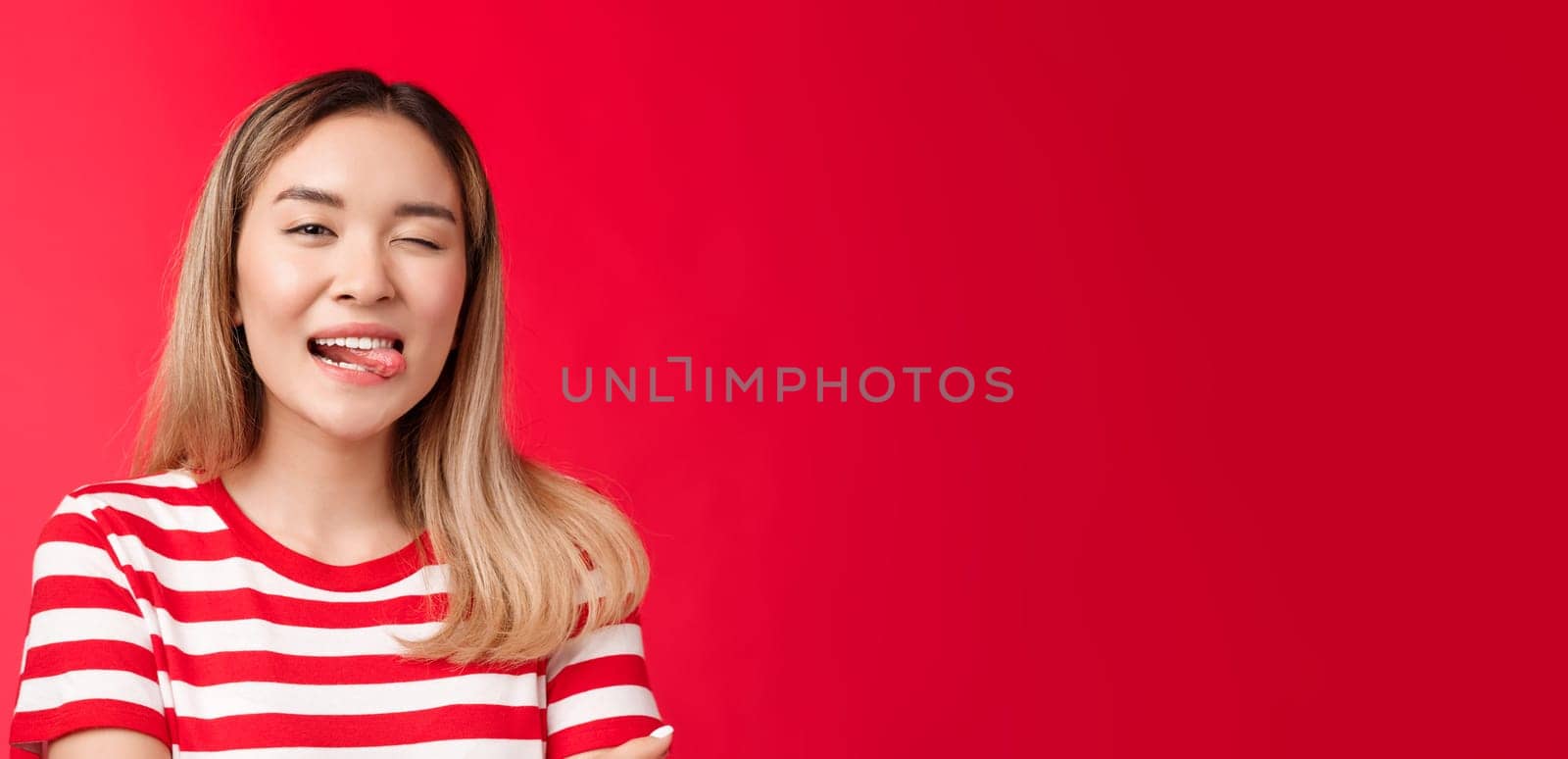 Close-up sassy carefree outgoing urban asian female student enjoy summer vacation wear striped t-shirt, show tongue playfully winking camera, stand red background positive friendly mood by Benzoix