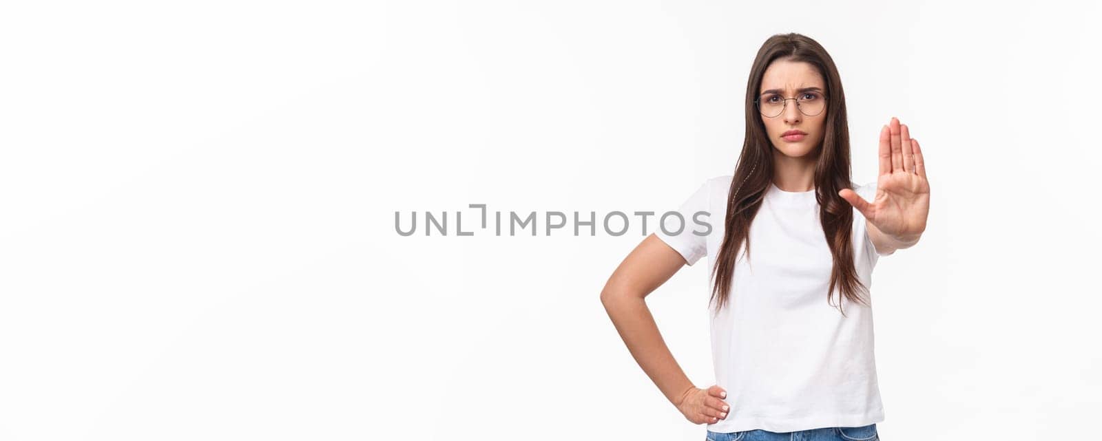 Waist-up portrait of serious-looking displeased confident young woman in glasses, activist or human-rights supporter pull palm forward to stop something bad, frowning disagree, prohibit action.