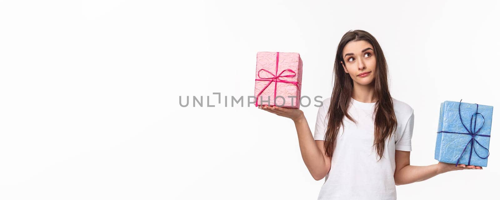 Celebration, holidays and presents concept. Portrait of thoughtful young girl taking decision, look up wondered, weighing gift boxes in hands spread sideways, what is heavier, white background.