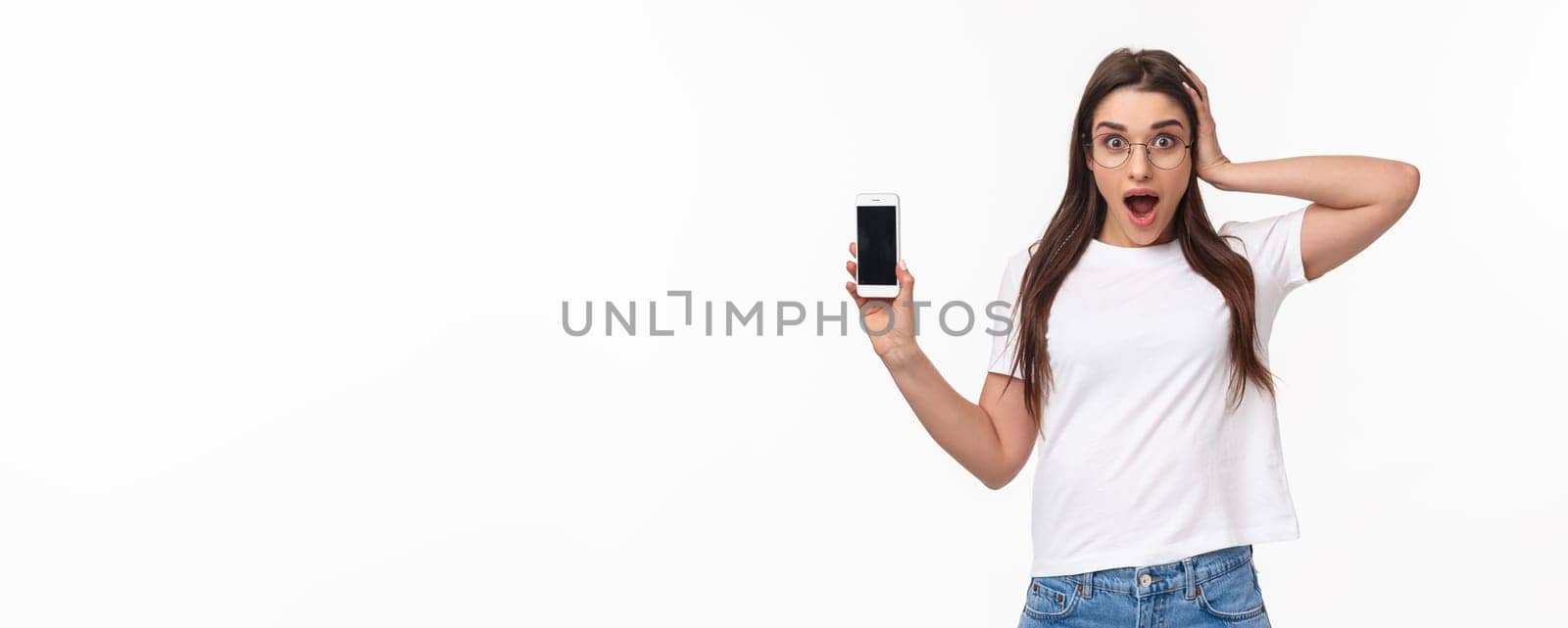 Communication, technology and lifestyle concept. Waist-up portrait of astonished surprised and excited young woman in glasses, gasping and touch head shocked as showing mobile phone awesome app by Benzoix