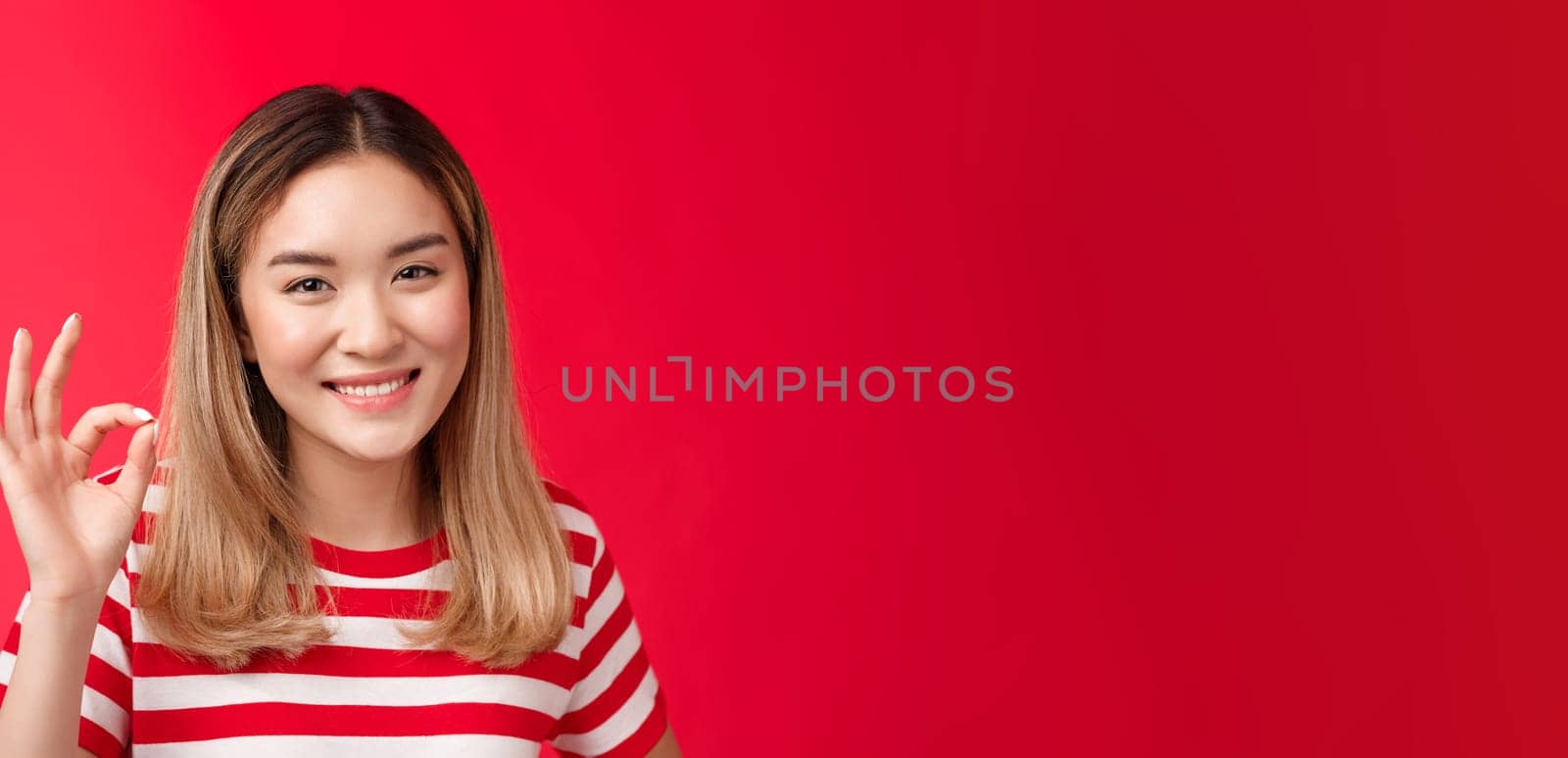 Close-up friendly satisfied carefree young asian blond girl show approval judgement sign okay ok, agree plan good smiling broadly like your idea satisfied great choice, stand red background glad by Benzoix