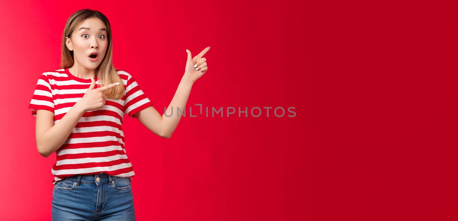 Surprised impressed attractive modern asian girl blond haircut open mouth gasping astonished, pointing right, show fingers impressive stunning promo new clothes collection look camera enthusiastic by Benzoix