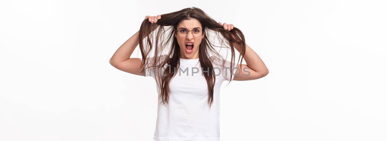 Waist-up portrait of bothered and annoyed, angry pissed-off young girlfriend losing temper, pulling hair from head and screaming being furious and outraged, white background.