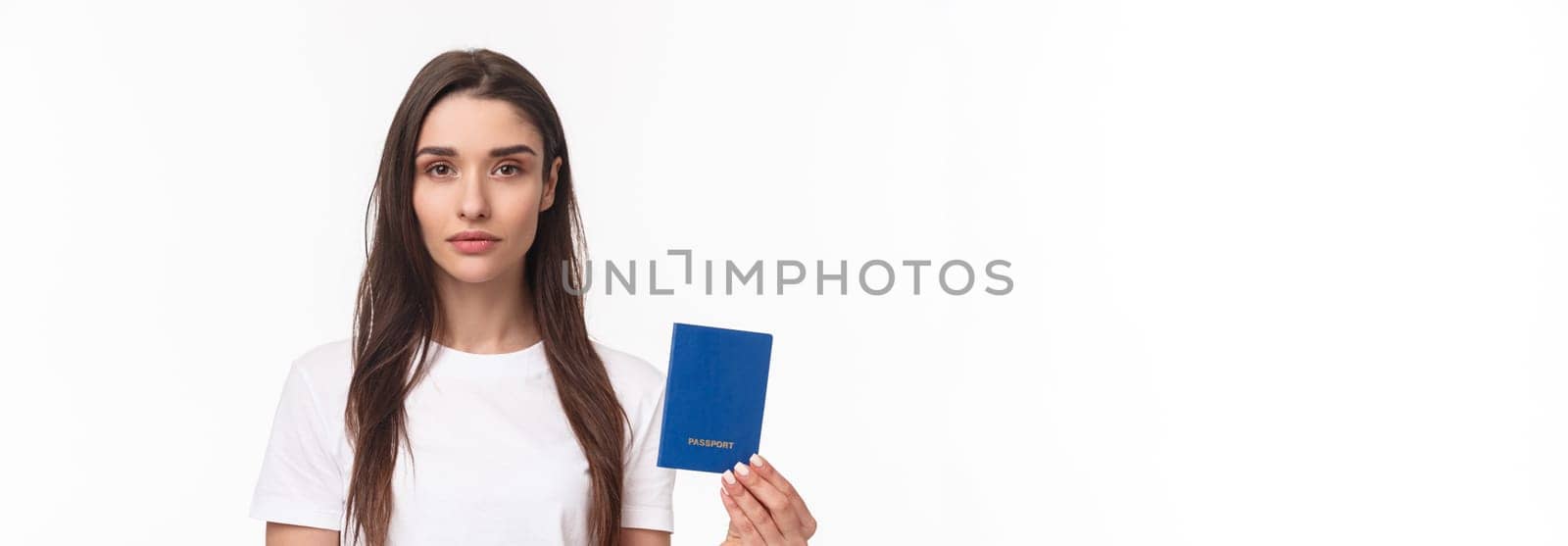 Travelling, holidays, summer concept. Serious-looking young confident girl showing her brand new passport, ready to travel abroad, packing up baggage, standing white background.