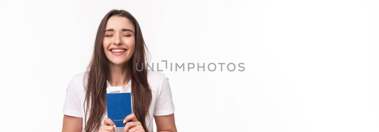 Travelling, holidays, summer concept. Close-up portrait of happy, dreamy girl feeling happy finally travel, holding passport with plane ticket, waiting in airport, standing white background.