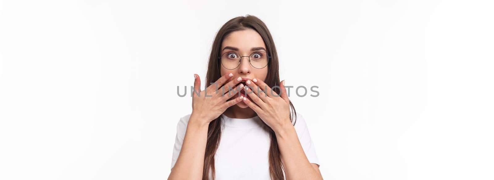 Close-up portrait of enthusiastic, shocked and amazed young happy girl hear awesome gossip, spilled tea, cover opened mouth with palms, express surprise with eyes, white background.