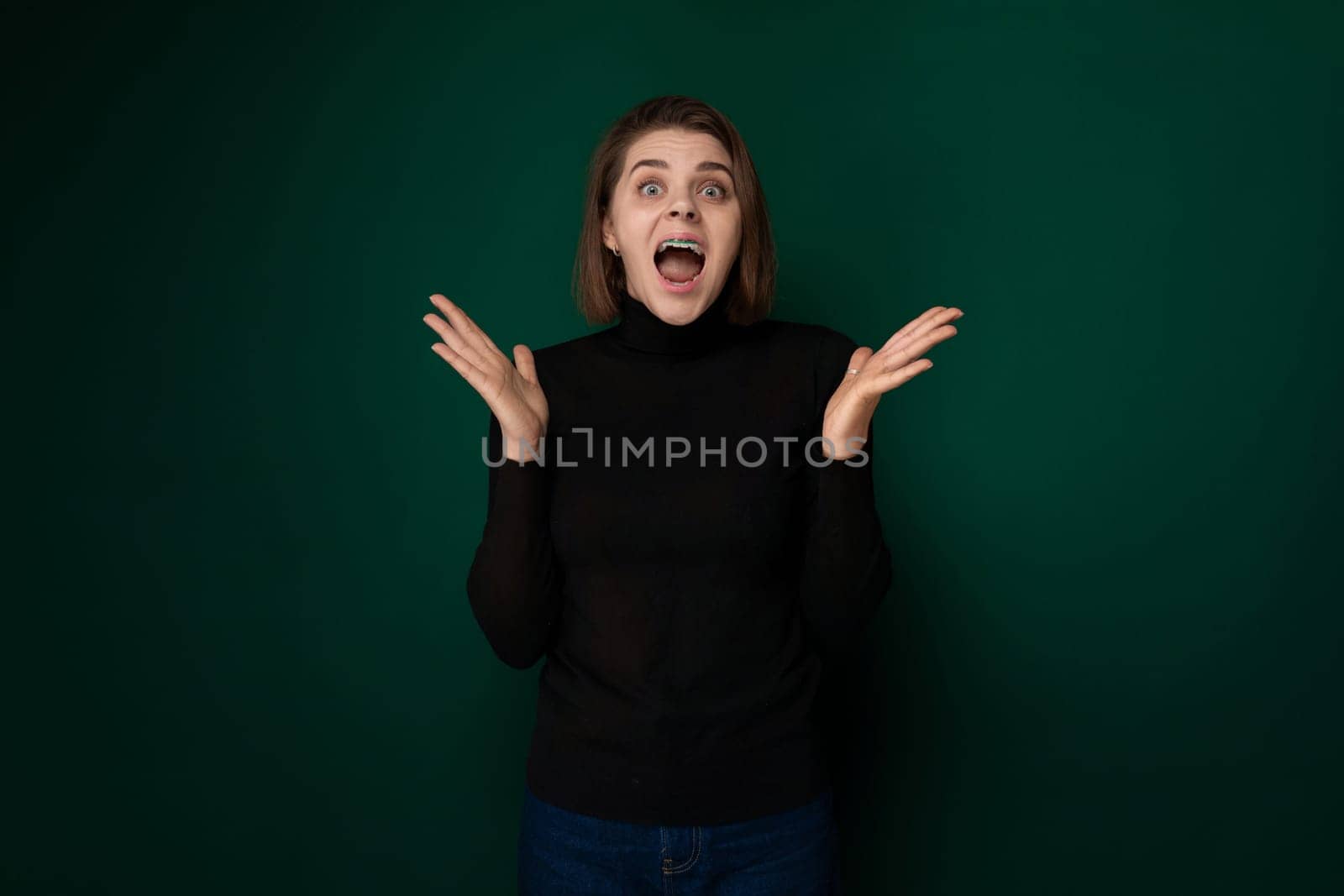 A woman wearing a black sweater is shown with a surprised expression on her face. Her eyebrows are arched, eyes wide open, and mouth slightly agape, indicating shock or disbelief.