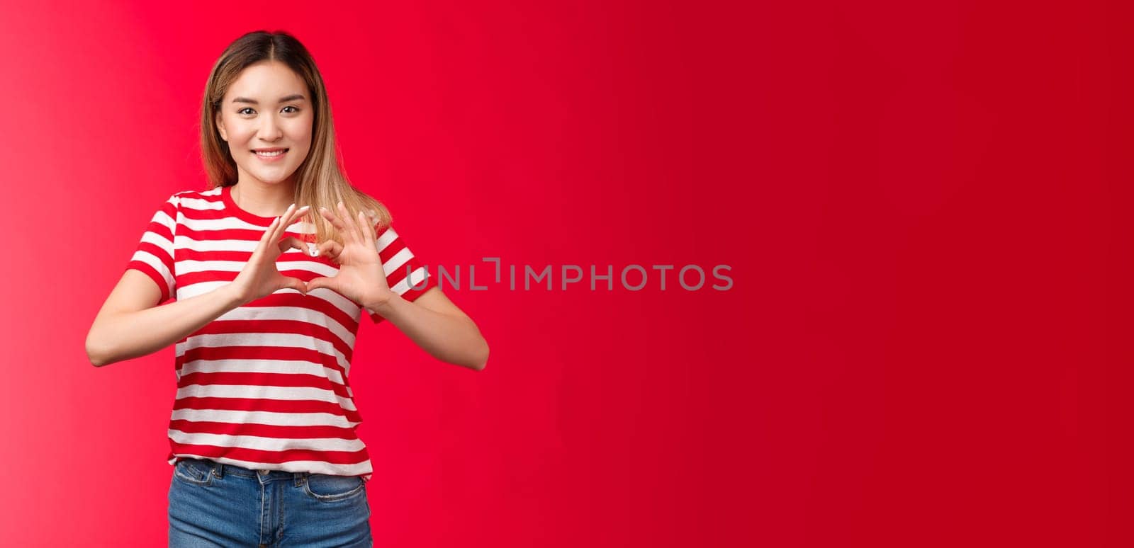 Asian girl express love and support lgbtq community. Heartwarming sweet tender blond female show heart sign near chest smiling friendly happily showing romantic attitude cherish relationship.