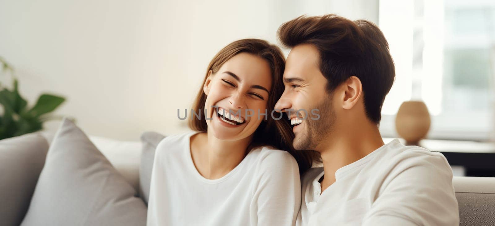 Portrait of happy smiling young couple hugging, cheerful woman and man sitting on sofa at home together