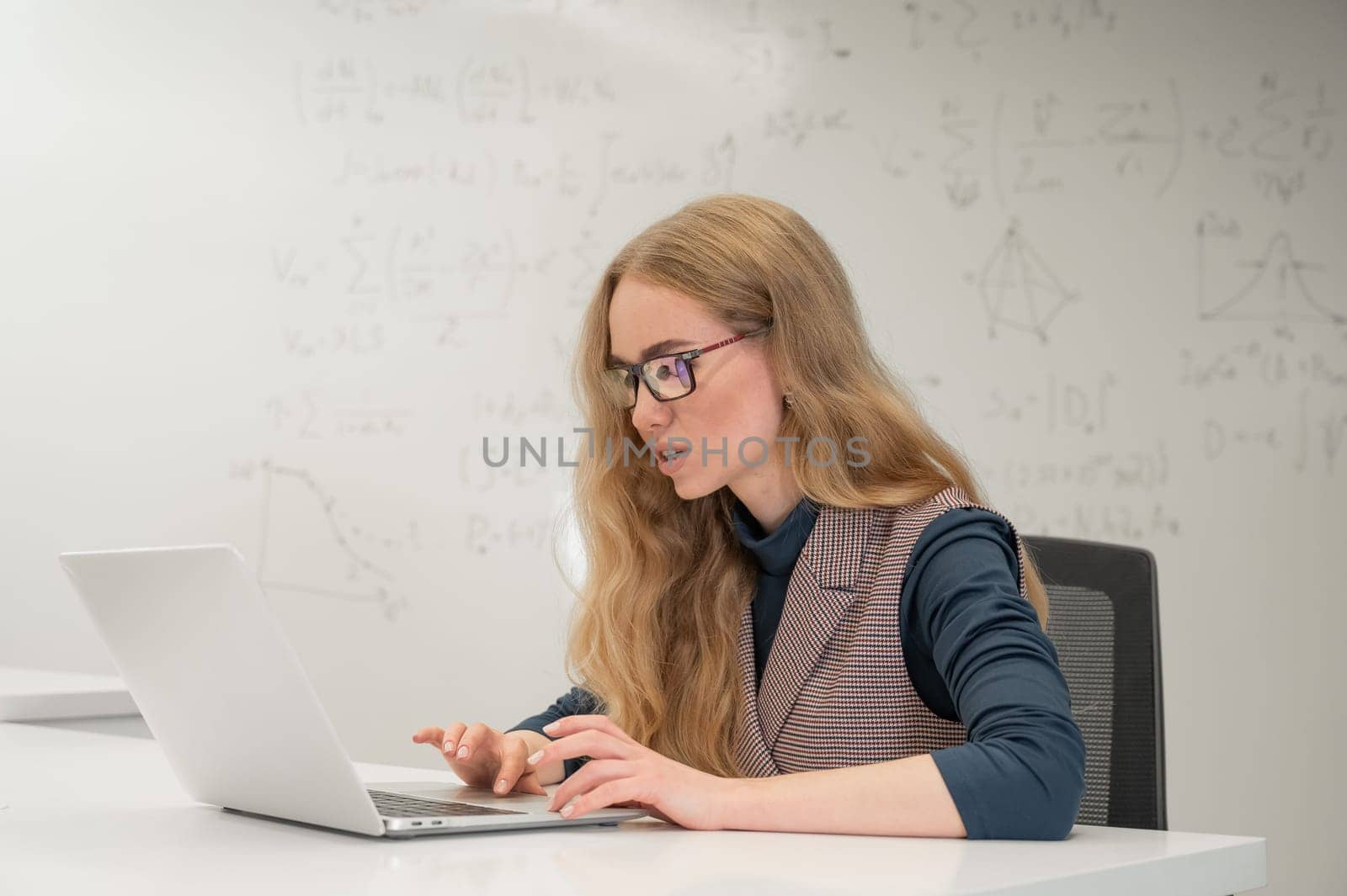 Caucasian woman scientist typing on laptop. White board with formulas