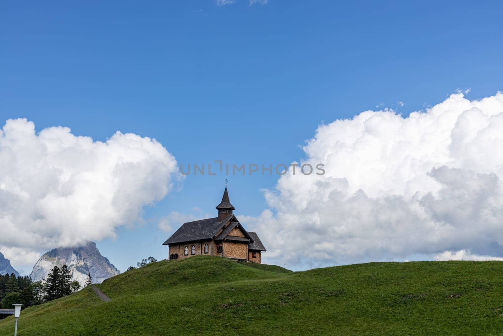 Beautiful view of the church standing on a green hill against the backdrop of mountains with clouds on a clear summer day in Fronalpstock Switzerland, close-up side view.