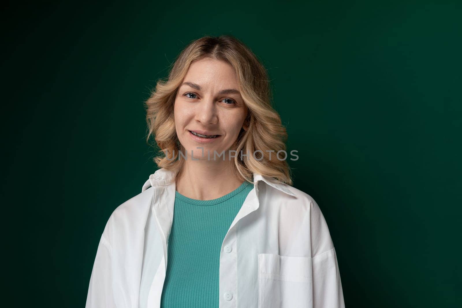 A woman wearing a white coat and a green shirt is standing outdoors.