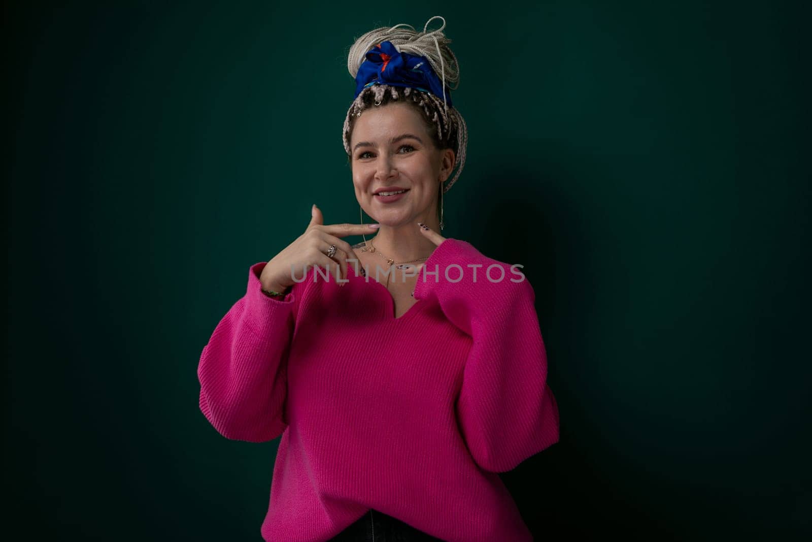 A woman wearing a pink sweater strikes a pose for a picture, looking directly at the camera with a confident expression. She stands in a casual yet stylish manner, exuding a sense of poise and charm.