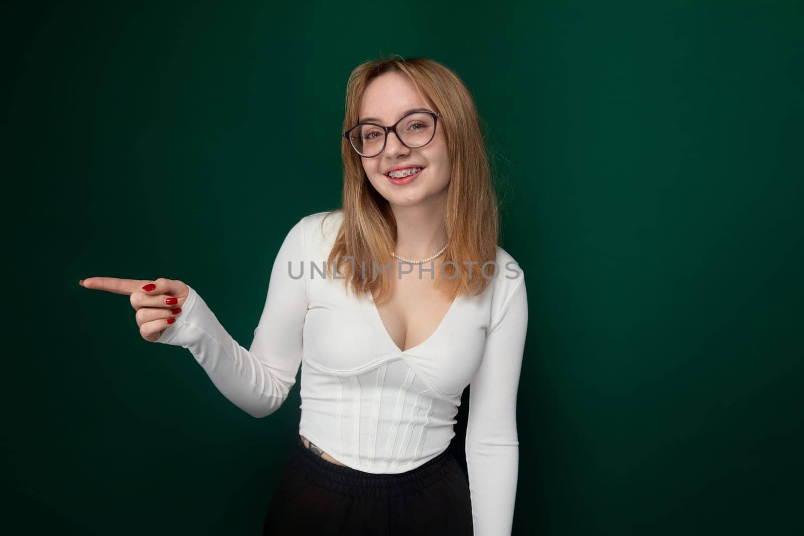 A woman with glasses is pointing at an unseen object or direction, indicating focus or interest in a specific topic or subject matter. She appears engaged and curious as she gestures towards the unseen point.