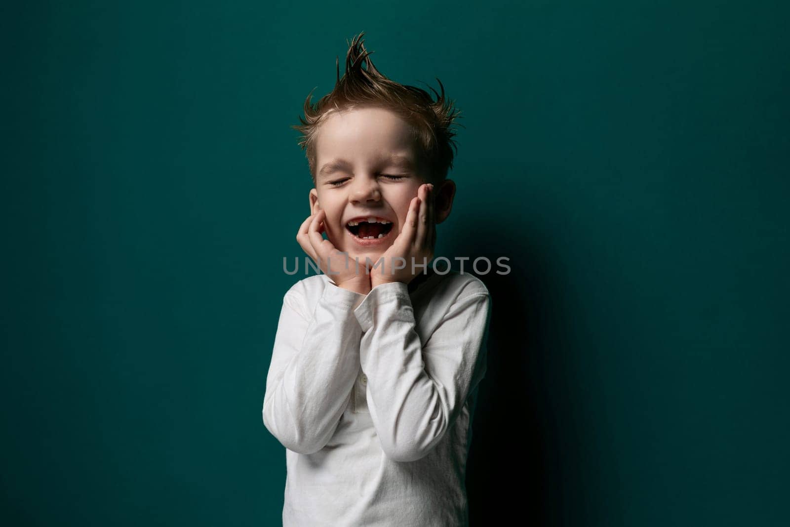 A young male child is standing in front of a vibrant green wall, looking straight ahead. He appears curious and engaged with his surroundings, with a slight smile on his face.