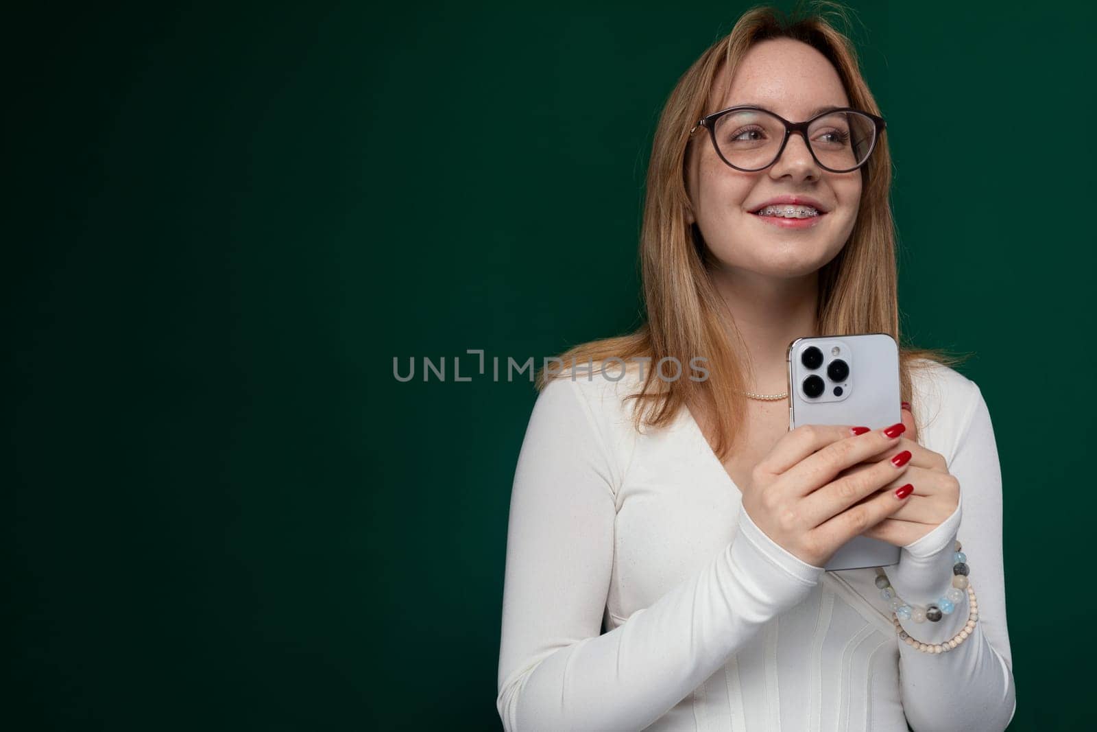 A woman wearing glasses is seen holding a cell phone in her hand. She appears to be looking at the screen intently, possibly texting or browsing. The background is blurred, placing the focus on the woman and her phone.