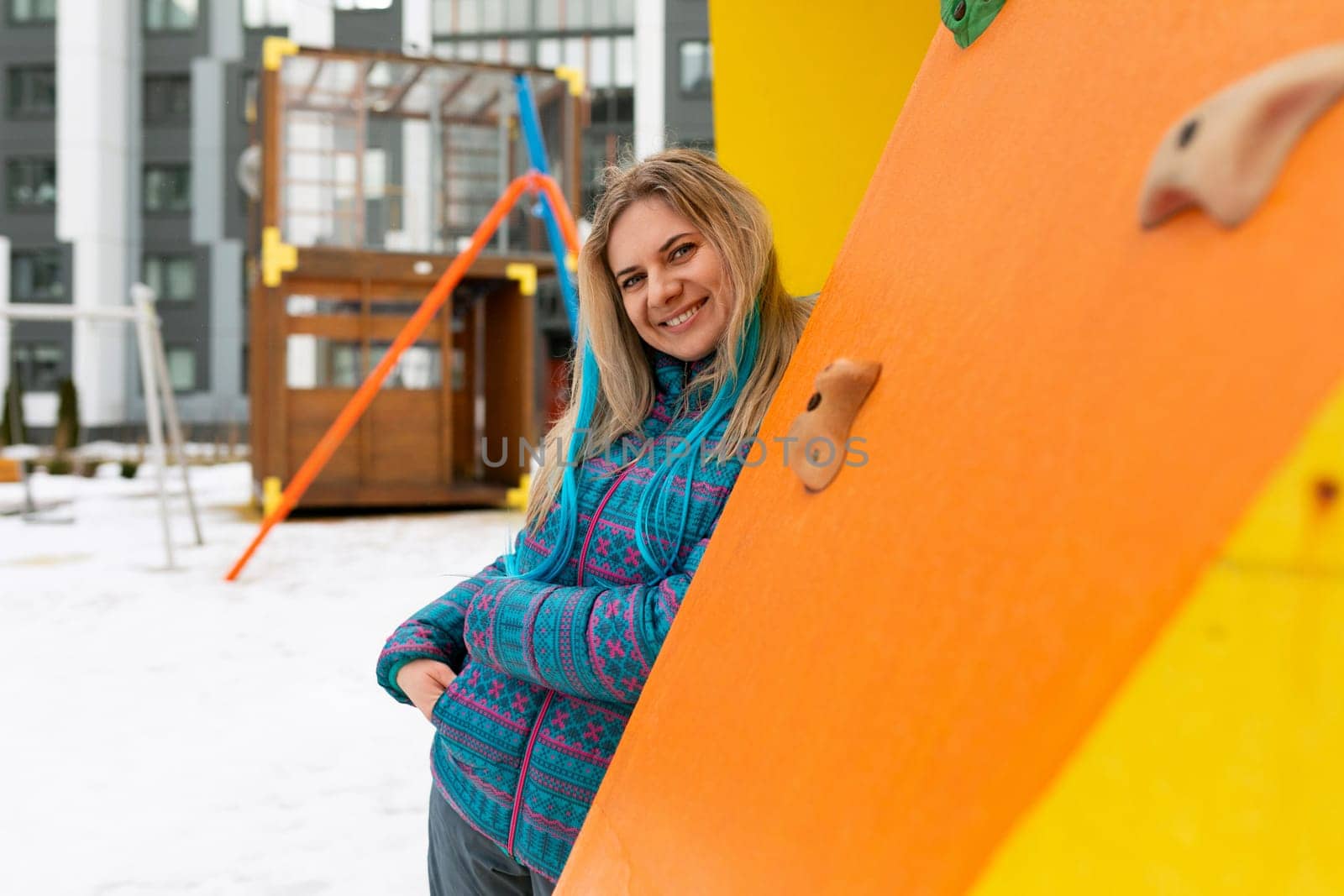 Blond woman in a blue winter jacket walks on the playground.
