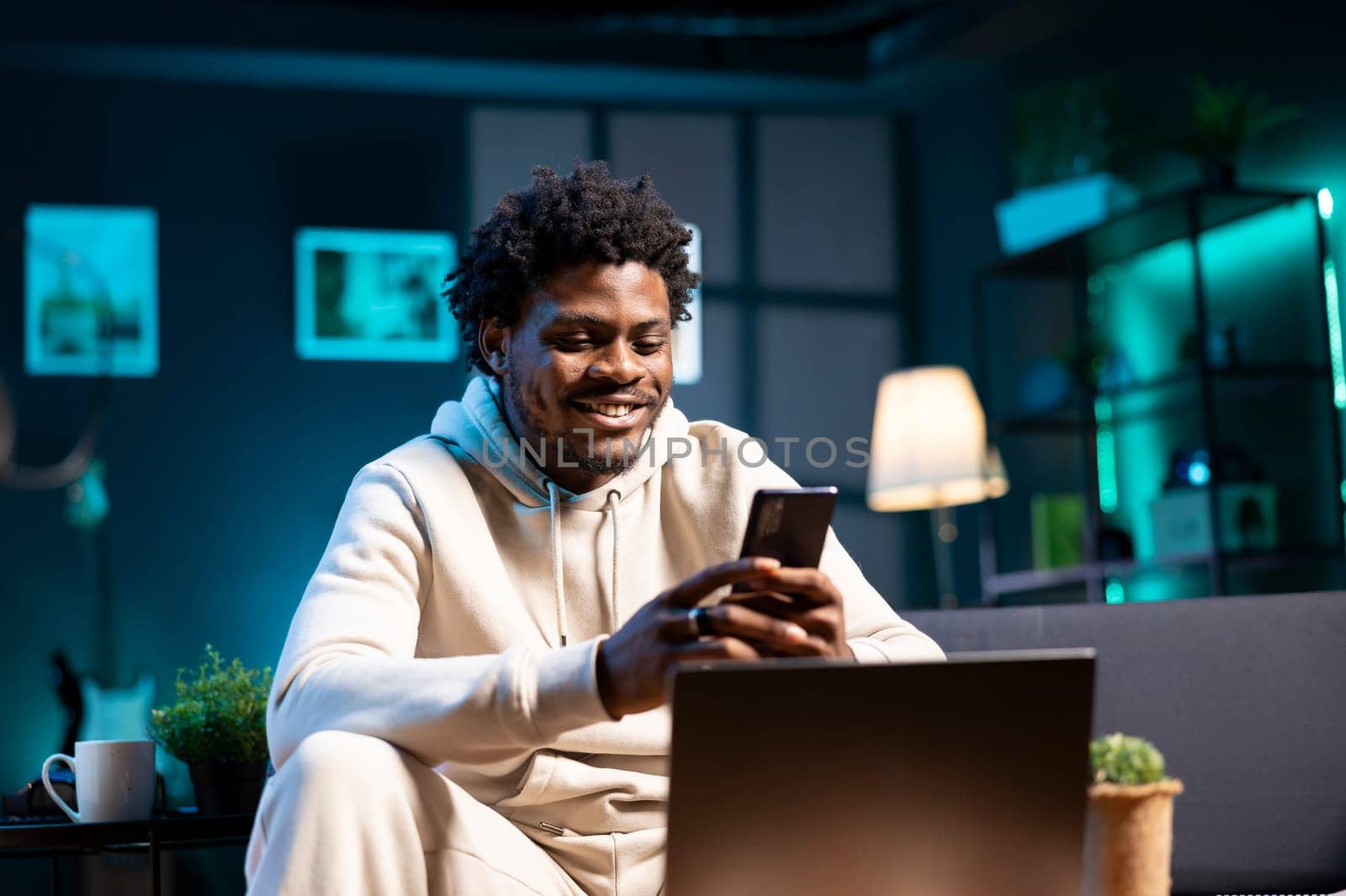 Smiling man at home taking break from work to write messages on phone. Joyous person holding cellphone talking with mates over online texting app before continuing project on laptop