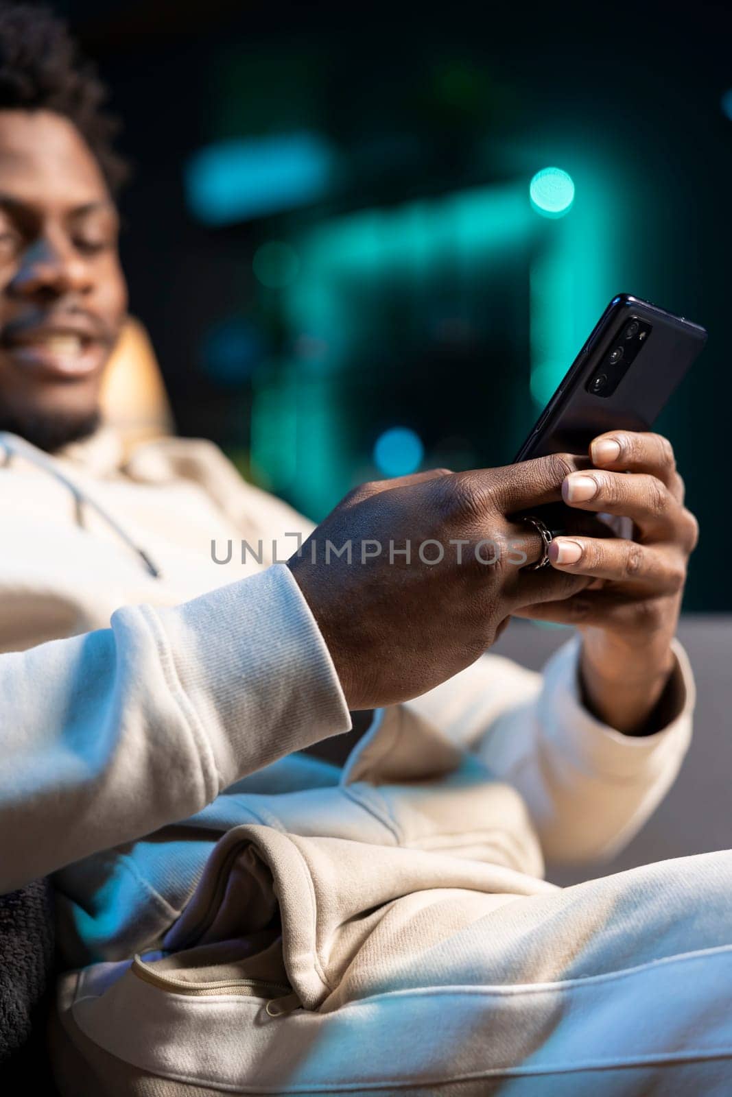 Focus on cellphone used by man in blurry background to compose messages, chatting with internet friends. Close up of mobile phone used by person to scroll on social media feed while in apartment