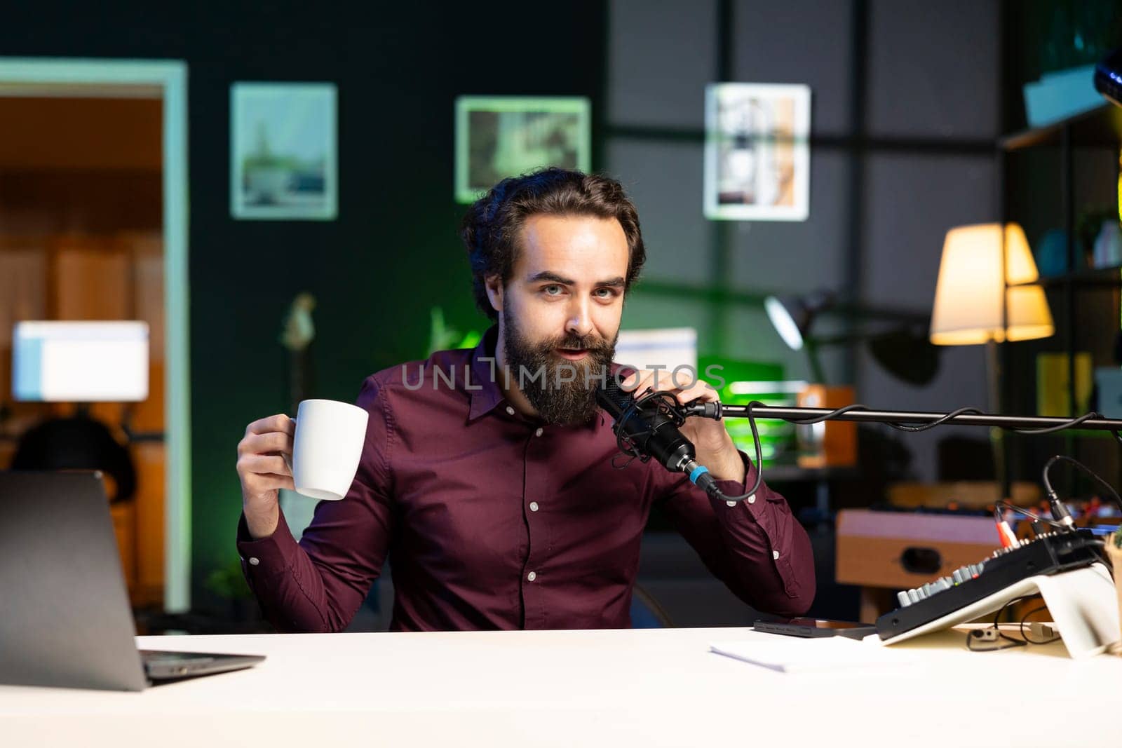Media star talking in professional microphone in studio at night and drinking coffee, filming internet video production. Content creator uses quality mic to speak to audience, enjoying hot beverage