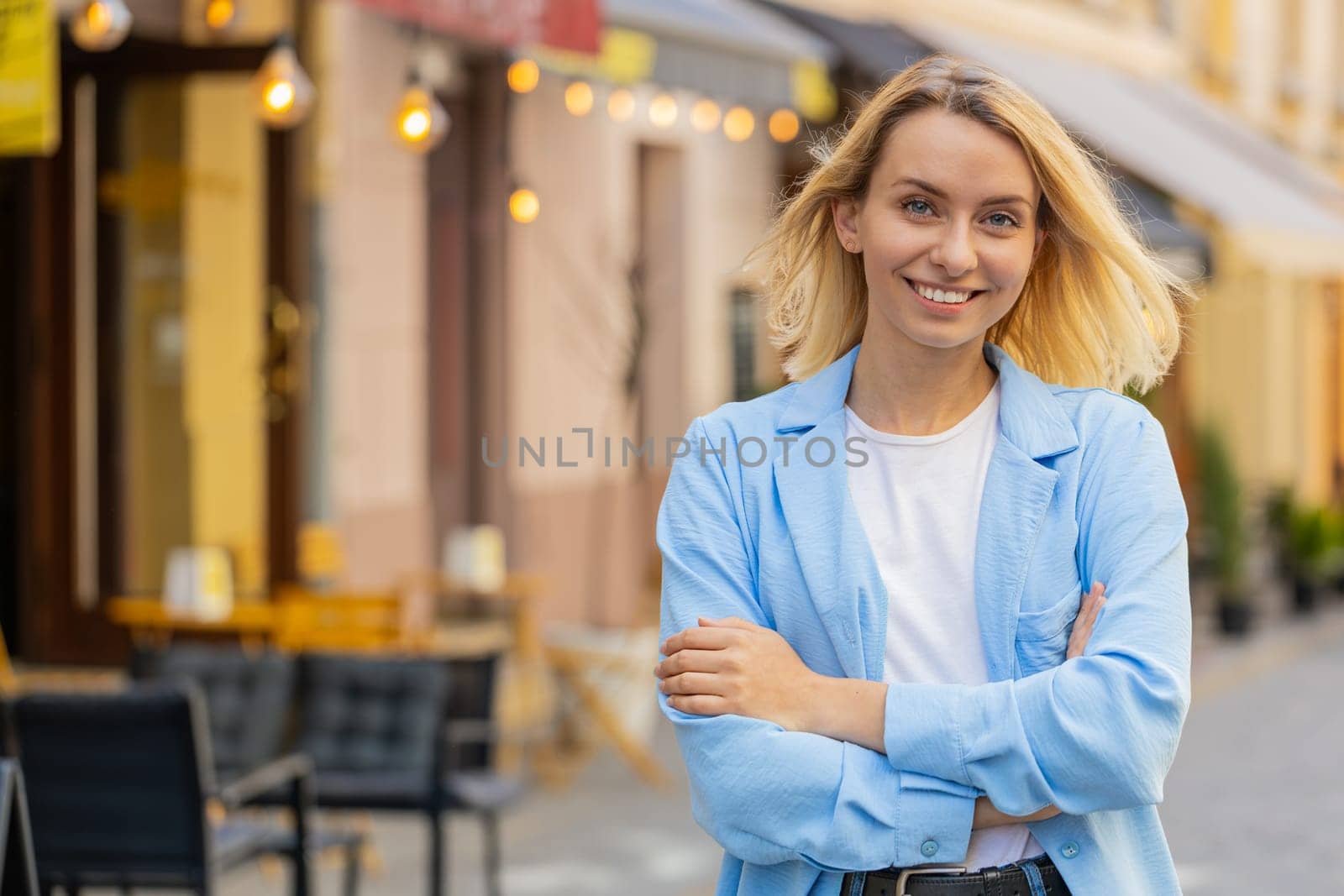 Portrait of happy young blonde woman friendly smiling glad expression looking at camera dreaming resting relaxation satisfied of good news outdoors. Lady standing on urban city street. Town lifestyles