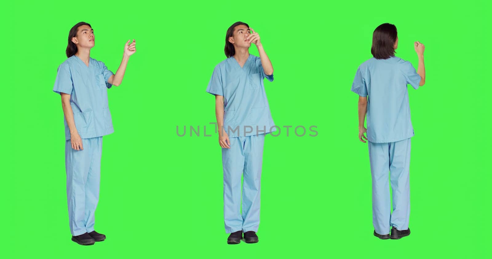 Asian medical nurse checks hologram in studio with greenscreen design, working with holographic icon tab and artificial intelligence. Male specialist in uniform with healthcare expertise.