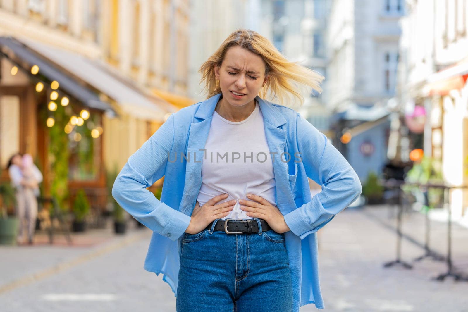 Caucasian young woman traveler feeling sudden strong abdominal stomach ache gastritis problem. Upset tourist lady having symptom poisoning diarrhea indigestion peptic ulcer pancreatitis on city street