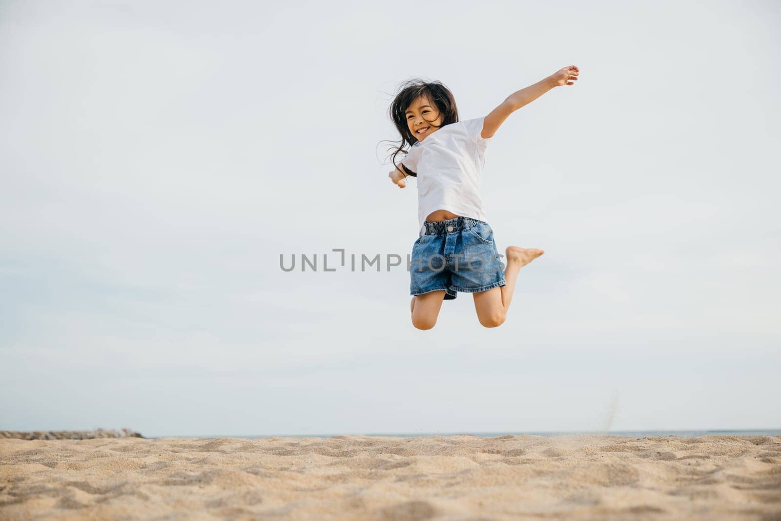 Portrait of a small girl jumping on the beach filled with joy and excitement. Playful motion vitality and the beauty of the Caribbean captured in this cheerful moment