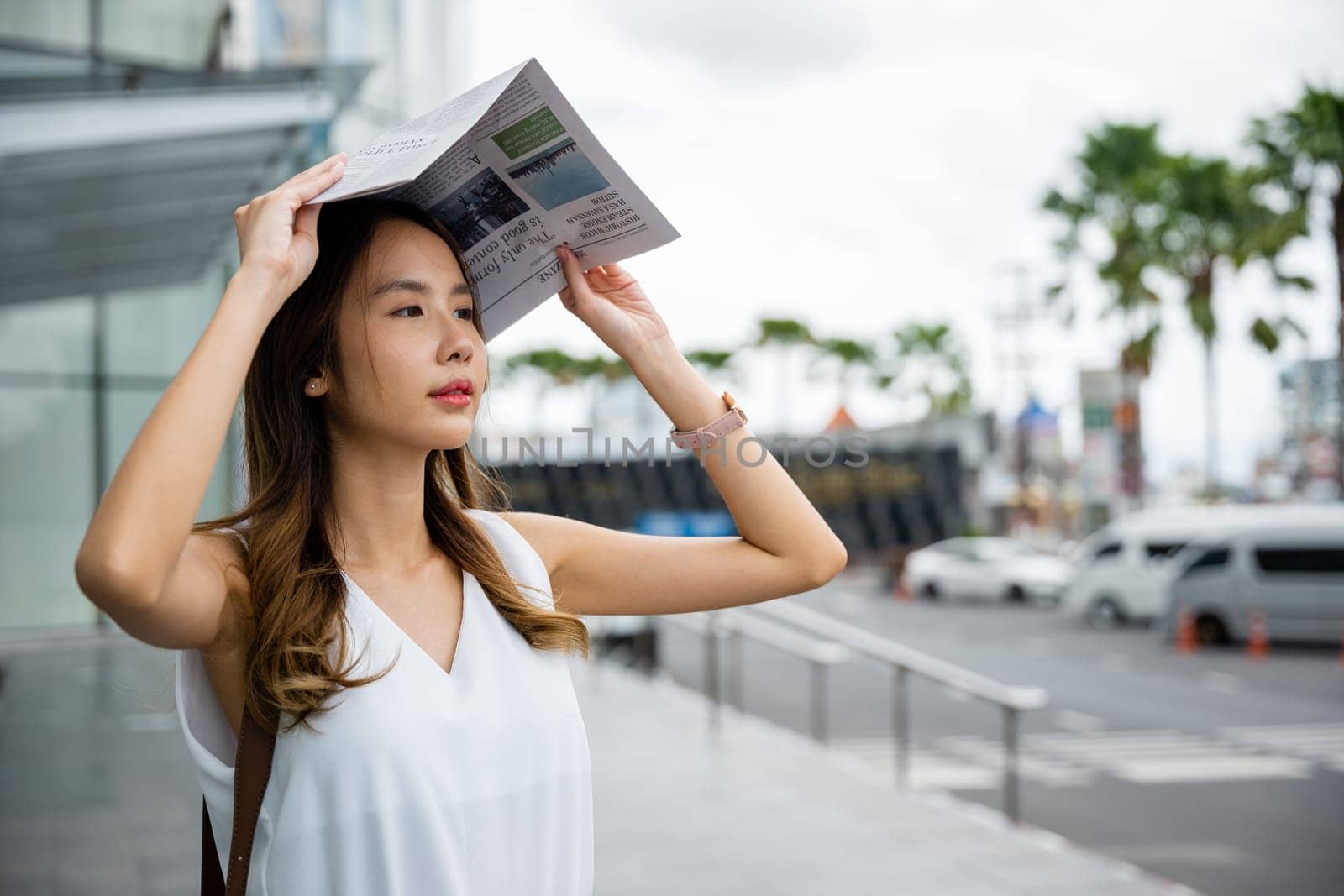 Overwhelmed by city living, an Asian woman covers her face with a newspaper by Sorapop